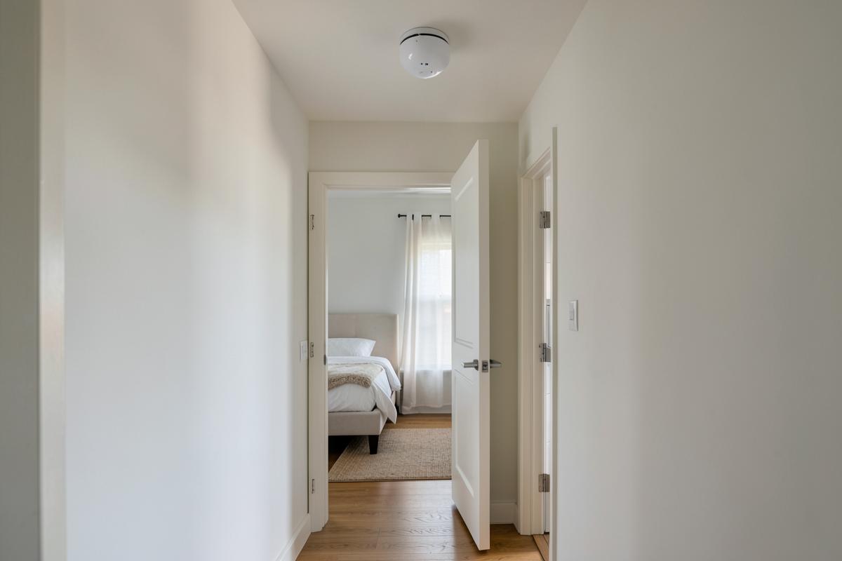 Ceiling-mounted smoke detector in a home hallway outside an open bedroom door