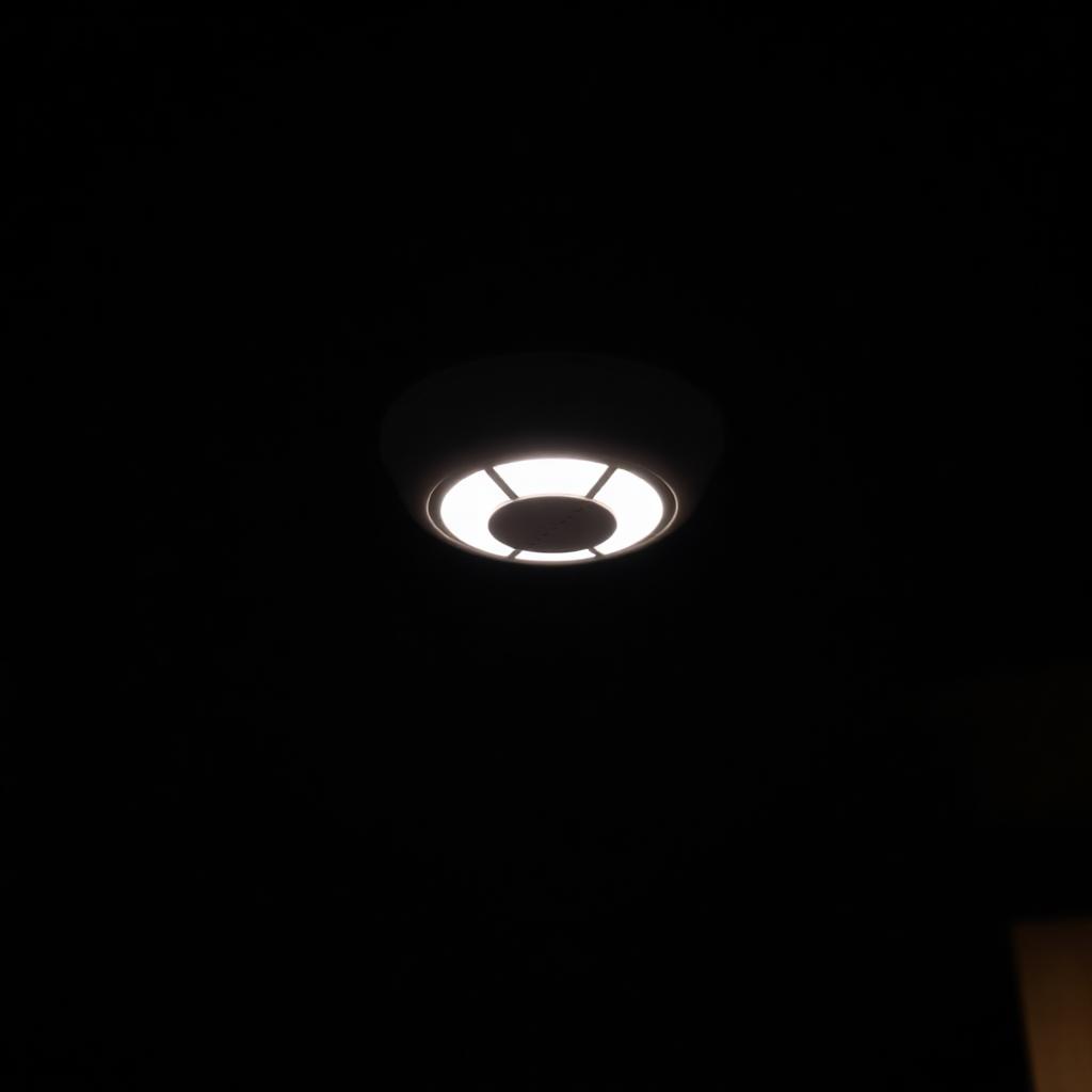 Small white smoke detector glowing softly on a ceiling at night
